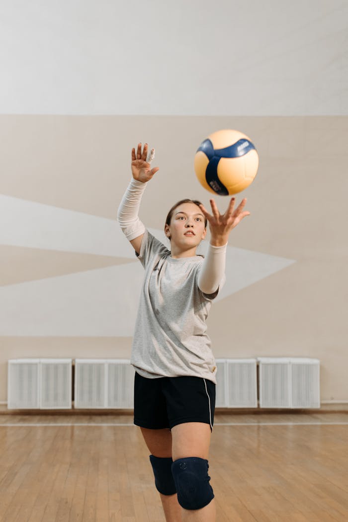 Focused woman volleyball player preparing to serve ball indoors during practice.