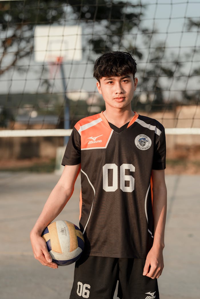 A confident young male volleyball player holding a ball on an outdoor court.